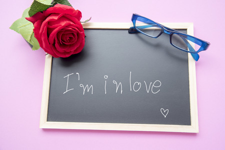 Red rose, blue glasses and blackboard on a pink blackboard.の写真素材