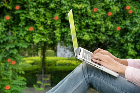 Young beautiful woman working outdoor in a public park. Working on laptop outdoors. Cropped image of female working on laptop while sitting in a park.の写真素材
