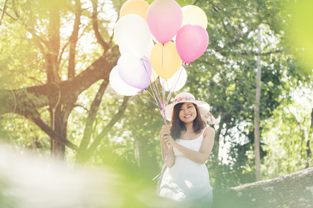 Beautiful young woman holding air balloons in gardenの写真素材