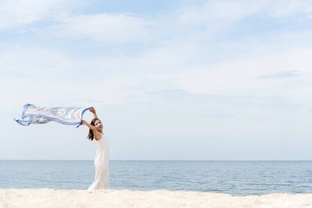 woman on the beach, portrait of young happy woman wearing white dress and holding scarf on tropical sand beach. Summer Concept.の写真素材