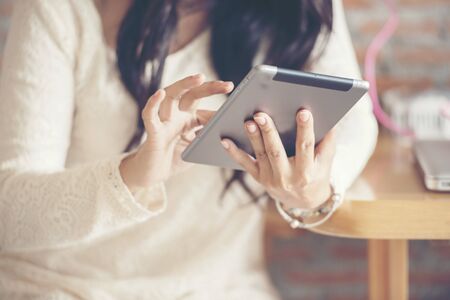 Beautiful young woman wear white lace dress using Ipad while sitting in coffee shop to explore website.の写真素材