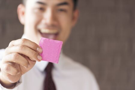 Handsome playboy showing condom on hand. Safe sex birth control concept.