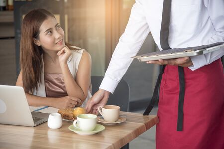 Beautiful business woman smiling looking at handsome waiter while serving food.の写真素材