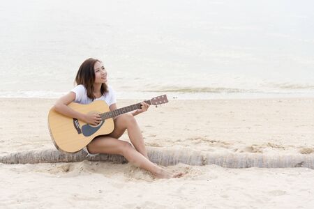 young woman playing guitar on the beach. Musician lifestyle. Travel concept.の写真素材