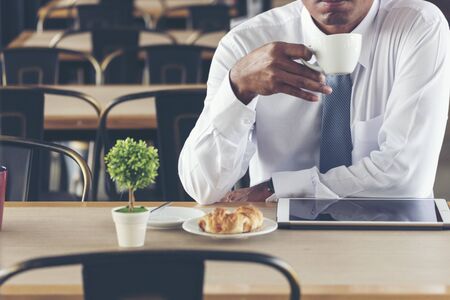 Asian Handsome businessman working outdoor in the coffee shop with laptop and holding cup of coffee on hand. Work outside office using technology with wifi, wireless connection. Technology Concept.の写真素材