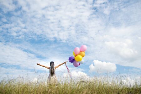 Happy woman jumping with air balloons on the meadow.の写真素材