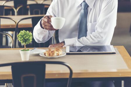 Asian Handsome businessman working outdoor in the coffee shop with laptop and holding cup of coffee on hand. Work outside office using technology with wifi, wireless connection. Technology Concept.の写真素材