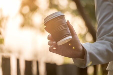 Closeup hand of beautiful woman holding a cup of coffee during sunrise.の写真素材