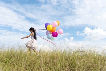Happy woman jumping with air balloons on the meadow.の写真素材