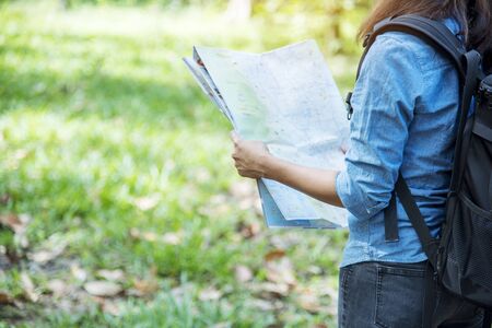 Woman traveller using map in green natural park trekking alone happy, carefree enjoy backpack...