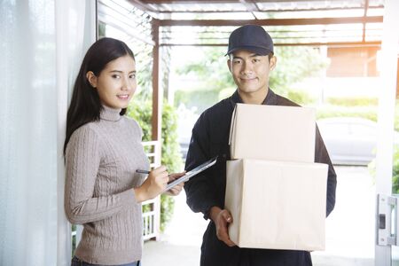Delivery mail shipping package services . Young deliveryman in uniform shipping goods package to recipient from shopping online and signing for got parcel package service on clipboard.の写真素材