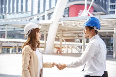 Construction engineer in Safety Suit Trust Team Holding White Yellow Safety hard hat Security Equipment on Construction Site. Hardhat Protect Head for Civil Construction Engineer. Engineering Conceptの写真素材