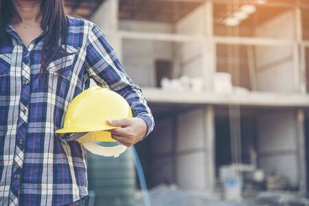 Woman engineer working on construction site and holding yellow hard hat safety helmet head protection at manufacturing industry. Construction Concept.の写真素材