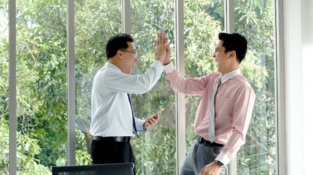 Success Businessman happy got good news from mobile smart phone that business so success. Asian young business man raise hand with happiness, smiling, excited after got great news from phone.の写真素材