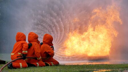 Firefighter fighting with flame using fire hose chemical water foam spray engine. Fireman wear hard hat, body safe suit uniform for protection. Rescue training in fire fighting extinguisherの写真素材