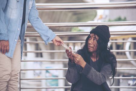 Woman helping hands to homeless people poverty beggar man holding hands asking for money job and hoping help in helpless dirty city sitting on streets. Desperate Beggar in city concept.の写真素材