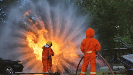 Firefighter fighting with flame using fire hose chemical water foam spray engine. Fireman wear hard hat, body safe suit uniform for protection. Rescue training in fire fighting extinguisherの写真素材