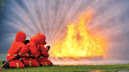 Firefighter fighting with flame using fire hose chemical water foam spray engine. Fireman wear hard hat, body safe suit uniform for protection. Rescue training in fire fighting extinguisherの写真素材