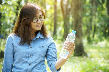 Healthy woman holding mineral drinking water in hands outdoor outside town in green park smile and looking at camera with happy face. Young woman happy outdoor lifestyle holding water bottle.の写真素材