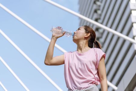 Sport Fitness Women drinking water in modern city wear wellness sportswear outside. Young woman workout outdoor exercising on bright sunny outside. Healthy wellness lifestyle woman concept.の写真素材