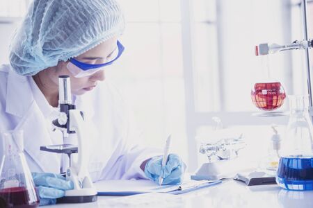 Female scientist look at microscope, science test tube analyse scientific sample in laboratory research experiment biotech make cultivate vaccine against virus. Chemistry science laboratory conceptの写真素材