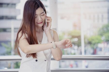 Asian woman calling smartphone look at watch. Happiness asian woman holding cellphone on call.の写真素材