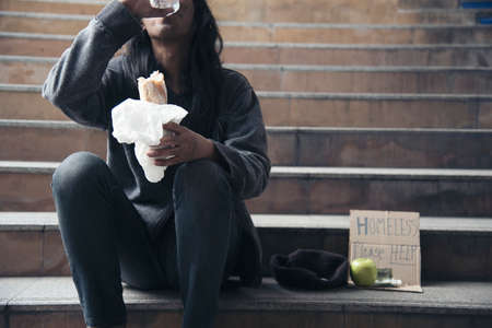 Homeless people poverty beggar man asking for money job and hoping help in helpless dirty city sitting with sign of cardboard box said "Homeless Please Help" on board. Beggar in city concept.の写真素材