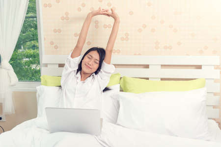 Beautiful woman stretching arm after working with laptop on bed.の写真素材