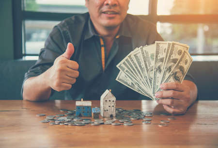 Investment Saving Money Concept. Businessman hold dollar bank note hand on budget to buy house real estate agent. Gold coins stack symbol buy property mortgage money loan with stack of money coinの写真素材