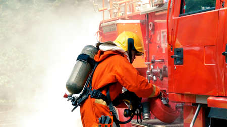 Firefighter fighting with flame using fire hose chemical water foam spray engine. Fireman wear hard hat, body safe suit uniform for protection. Rescue training in fire fighting extinguisherの写真素材