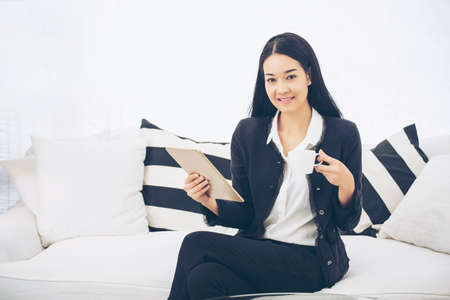 Working beautiful woman sitting on black and white sofa  using technology with smart tablet modern lifestyle. searching internet and online shopping. Technology Concept.の写真素材