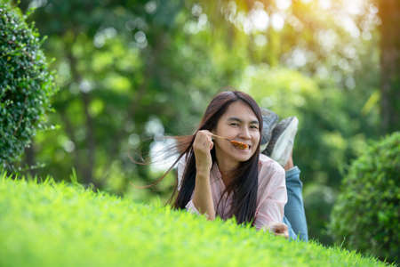 Relax beautiful asian woman smiling face Lying down on green grass field in outdoors garden park enjoy nature morning. Freedom Lifestyle woman breathing fresh air in green park on spring lawn outdoorsの写真素材