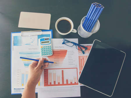 Woman working at home office desk using laptop business financial document chart and graph on wooden table with coffee cup. Woman freelance reading business graphs sale report on business office deskの写真素材