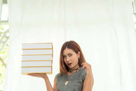 Young Asian Woman student university holding text book on her hands sitting on sofa with colorful pillow. Study hard to get a better grade. Education Conceptの写真素材