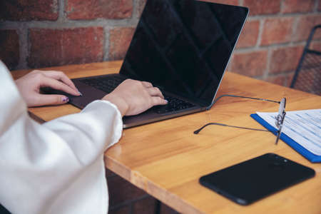 Woman working at home office desk using laptop business financial document chart and graph on wooden table with coffee cup. Woman freelance reading business graphs sale report on business office deskの写真素材
