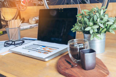 Office laptop business financial document chart and graph on wooden table with coffee cup. Flat lay notebook computer laptop on office desk. No people business graph chart mockup on business workspaceの写真素材