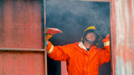 Firefighter fighting with flame using fire hose chemical water foam spray engine. Fireman wear hard hat, body safe suit uniform for protection. Rescue training in fire fighting extinguisherの写真素材