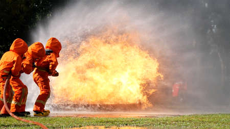 Firefighter fighting with flame using fire hose chemical water foam spray engine. Fireman wear hard hat, body safe suit uniform for protection. Rescue training in fire fighting extinguisherの写真素材