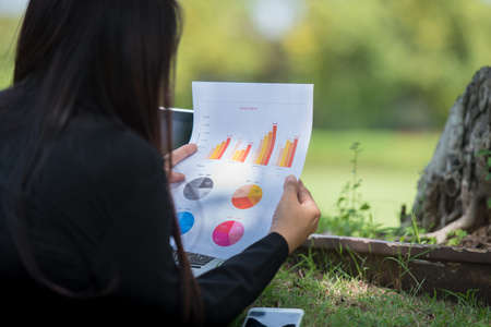 Asian entrepreneur business woman reading business graph analyze chart using laptop on green garden...
