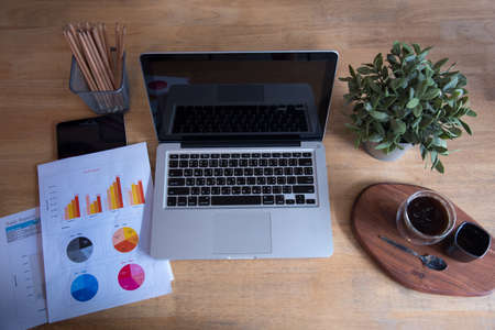 Office laptop business financial document chart and graph on wooden table with coffee cup. Flat lay notebook computer laptop on office desk. No people business graph chart mockup on business workspaceの写真素材