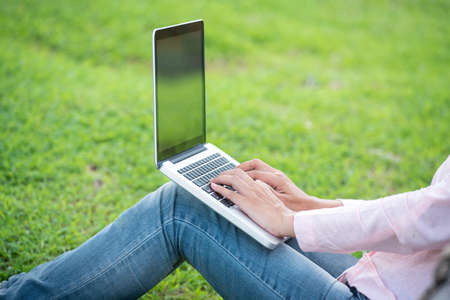 Asian woman sitting green park using laptop computer. Woman working on laptop happy entrepreneur...