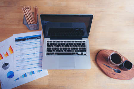 Office laptop business financial document chart and graph on wooden table with coffee cup. Flat lay notebook computer laptop on office desk. No people business graph chart mockup on business workspaceの写真素材