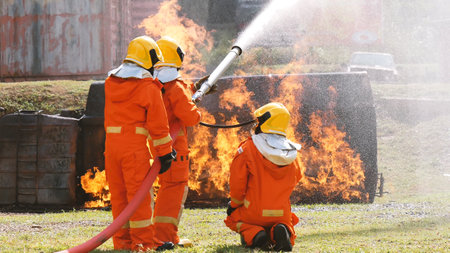 Firefighter fighting with flame using fire hose chemical water foam spray engine. Fireman wear hard hat, body safe suit uniform for protection. Rescue training in fire fighting extinguisherの写真素材