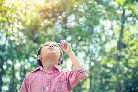 Adorable happy cute girl playful foam bubbles in green playground in summer outdoors. Funny Cheerful...