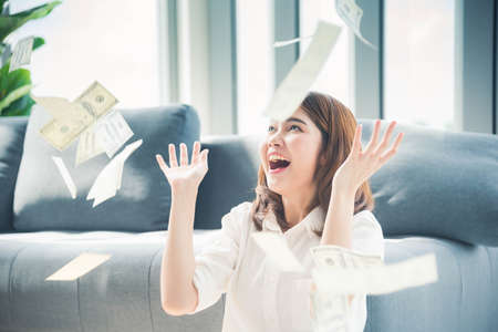 Happy young asian woman holding dollar money and throw in the air celebrate happiness dance wealth lottery money rain drop. Winner Success business woman throw cash flow Happy money smiling faceの写真素材