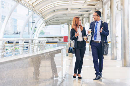 Businessman Businesswoman drinking coffee in town using smartphone outside office modern city. Hands holding take away coffee cup and smart phone talking together Business partner with cup of coffeeの写真素材