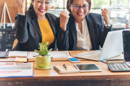 Happy success business woman partner working together in company office corporate executive teamwork. Meeting Executive Asian business woman using laptop office desk with fist arm raised win happinessの写真素材
