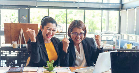 Happy success business woman partner working together in company office corporate executive teamwork. Meeting Executive Asian business woman using laptop office desk with fist arm raised win happinessの写真素材