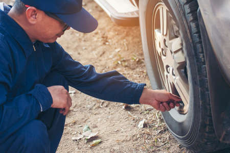 Mechanic man hands checking car tires outdoor on site service auto garage for automotive mobile center services. Technician workshop repair checking tyres car motor vehicles service mechanical handsの写真素材