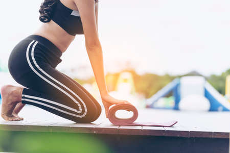 Woman hands rolled up yoga mat outdoor workout. Close up hands rolling foam yoga gym mat outside morning exercise. Woman stretching workout sportive healthy lifestyle on street city town park conceptの写真素材